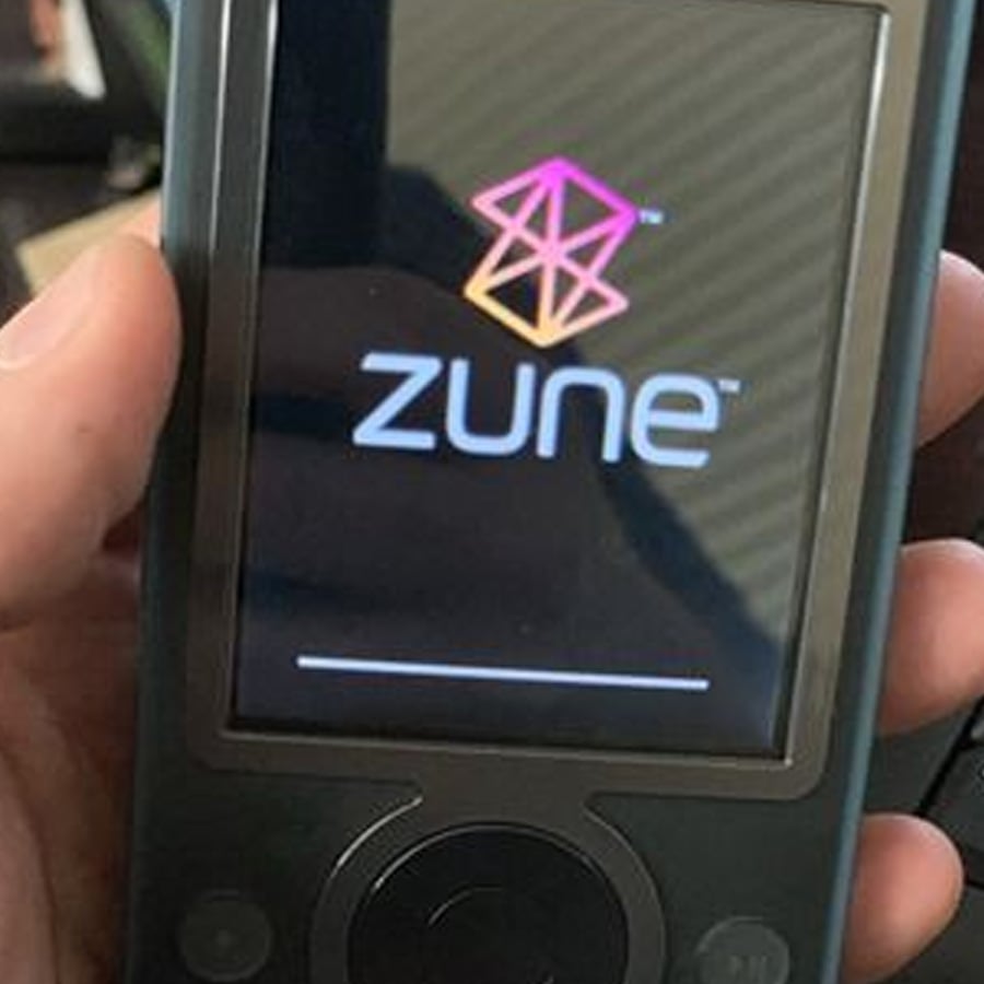 A hand holding a Microsoft Zune media player, displaying the Zune logo and loading screen on its display.