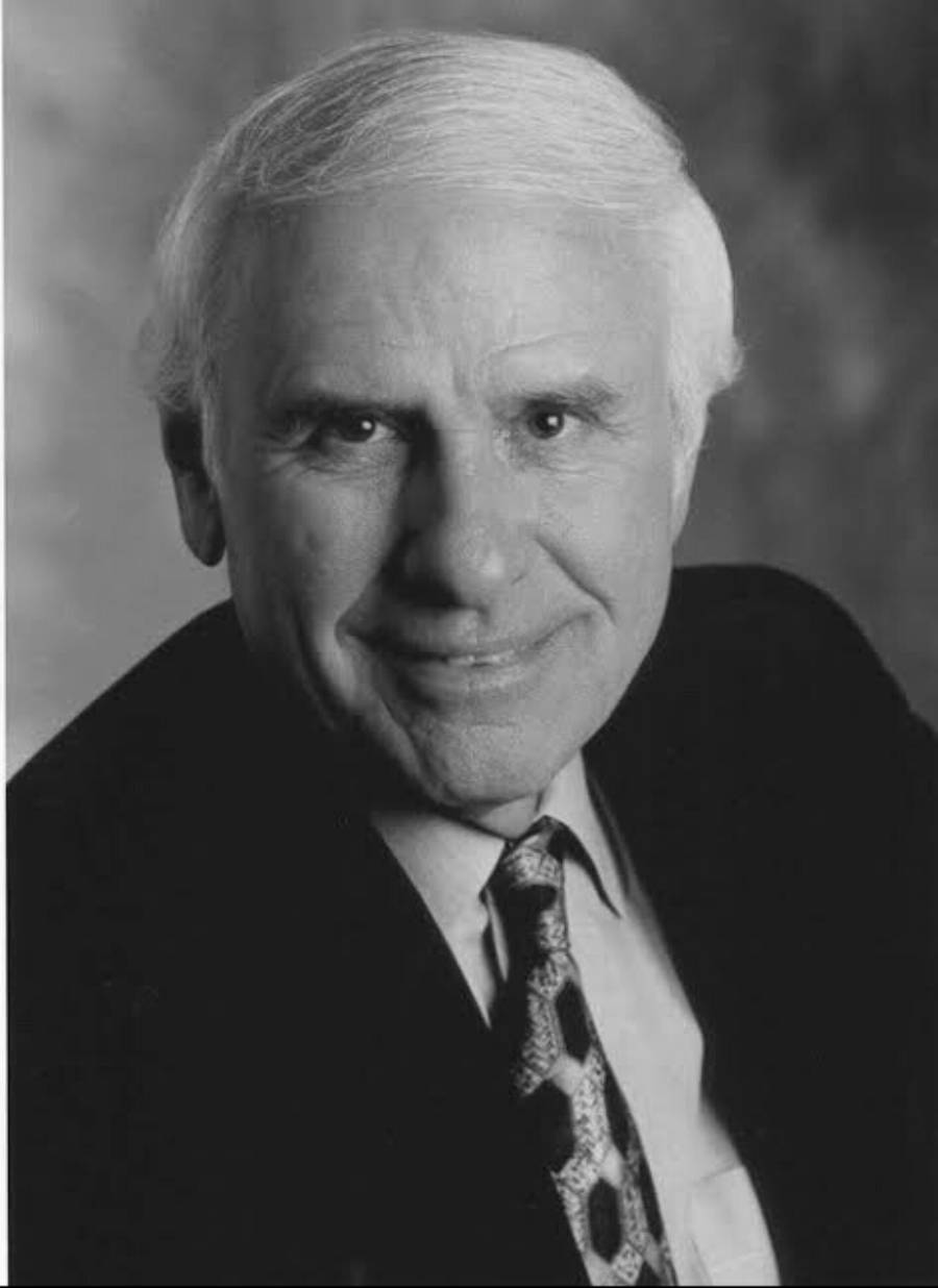 Black and white portrait of an older man with white hair, wearing a suit and patterned tie, smiling slightly while looking at the camera, with a soft-focus background.