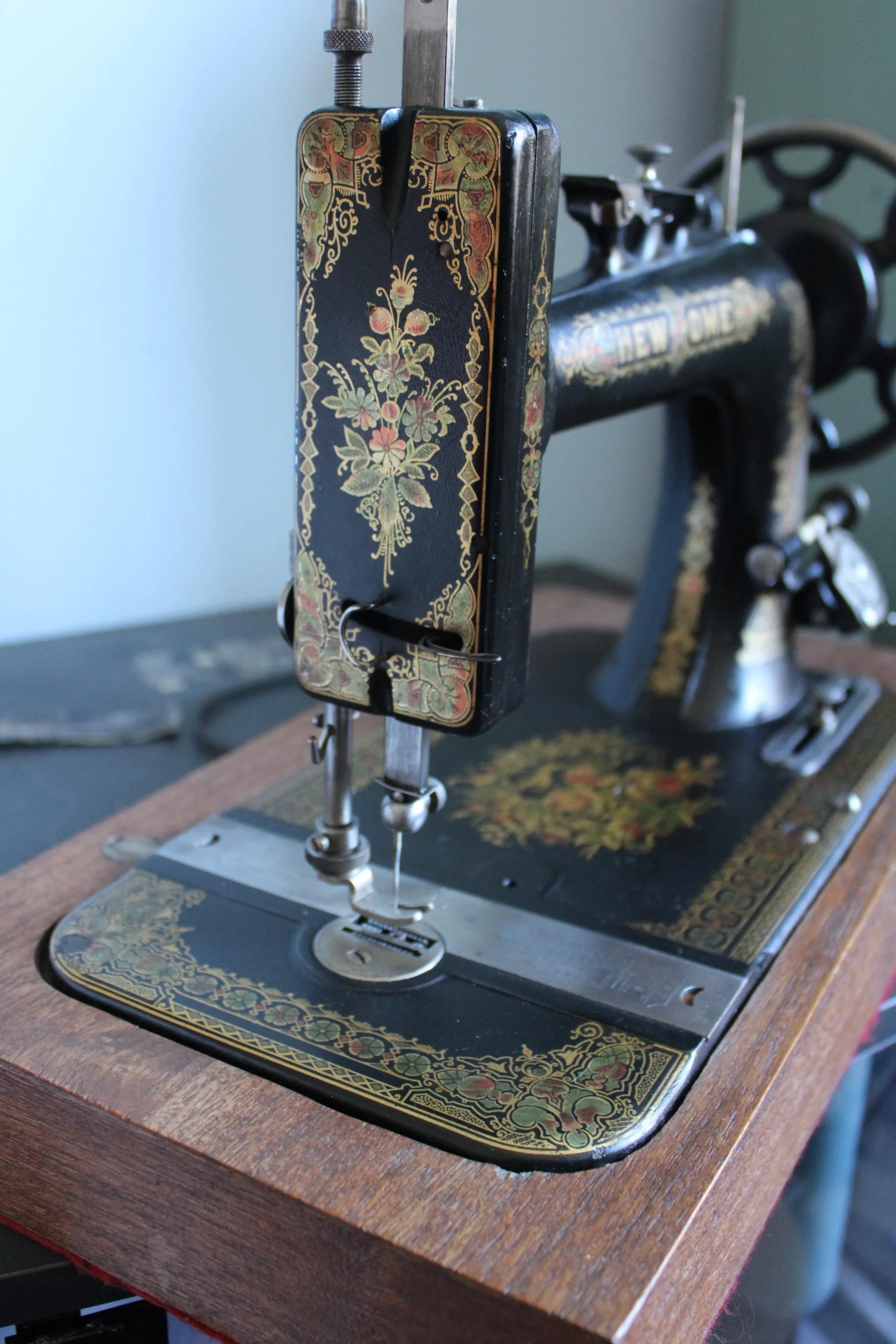 A close-up of a vintage black sewing machine with ornate gold floral designs, set on a wooden base.