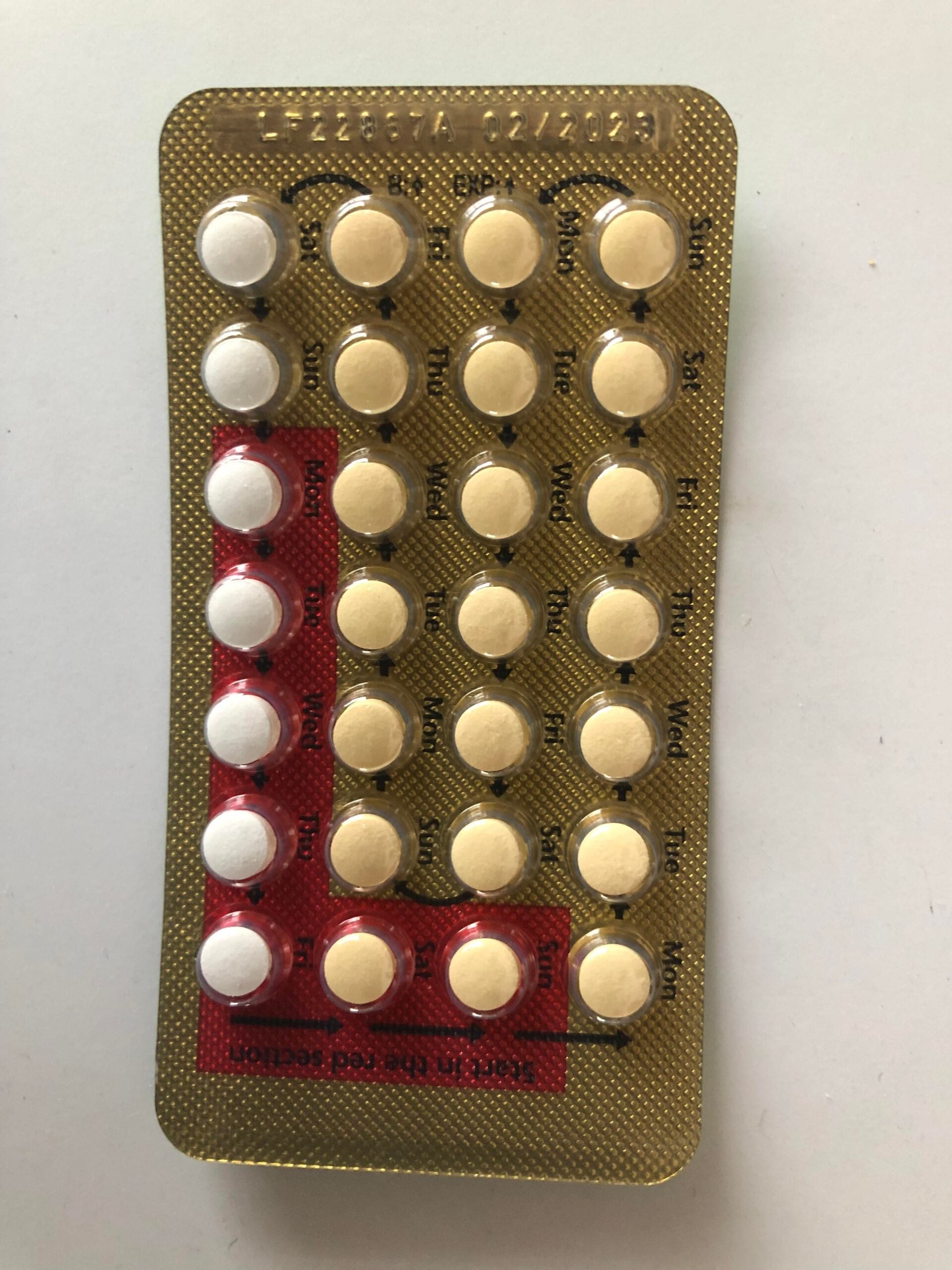 A blister pack of birth control pills with 28 tablets, including 7 white and 21 yellow pills, arranged in rows labeled with days of the week.