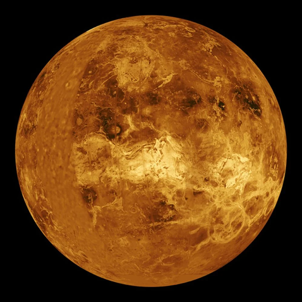 A detailed, golden-yellow image of planet Venus shows its cloudy, textured surface against a black background. The surface appears rough with light and dark areas.