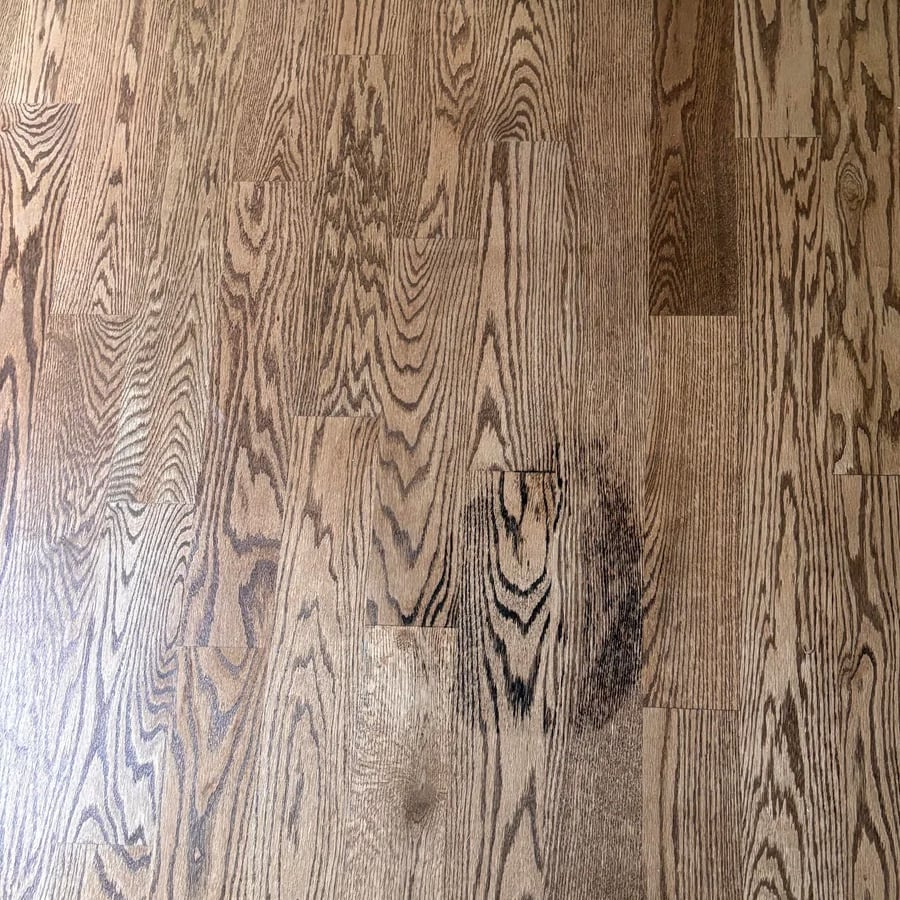 Close-up view of a wooden floor with distinct, varied grain patterns and shades of brown, showcasing the natural texture and character of the wood planks.