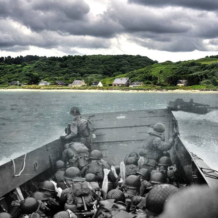 A faded WWII photo of soldiers landing on a beach is blended with a modern color photo of the same spot, showing green hills, houses, and cloudy skies.