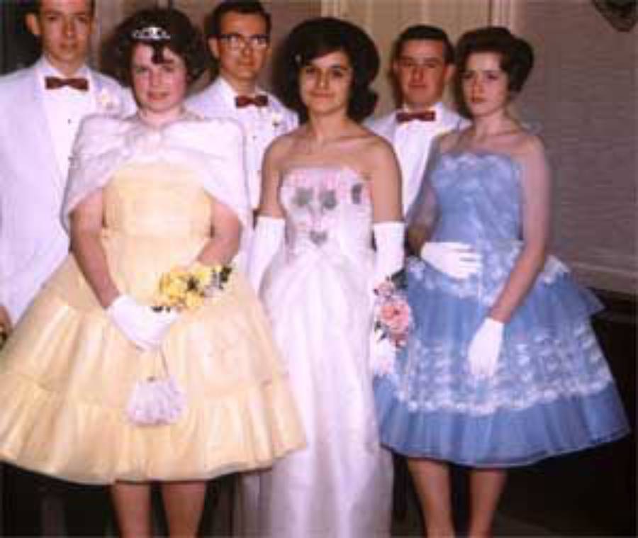 A group of young people in formal attire pose for a photo; three women wear colorful dresses and gloves, while three men wear suits and bow ties. It appears to be a prom or formal dance from the mid-20th century.