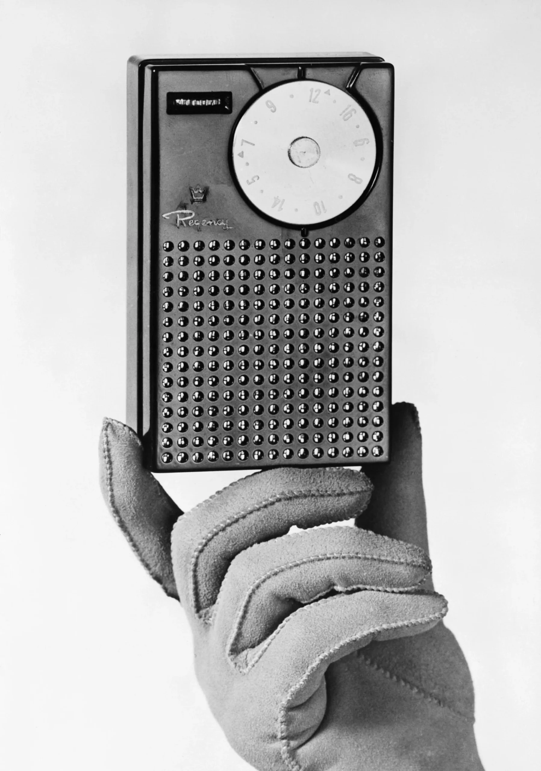 A gloved hand holds a vintage transistor radio with a large tuning dial and a perforated speaker grille.