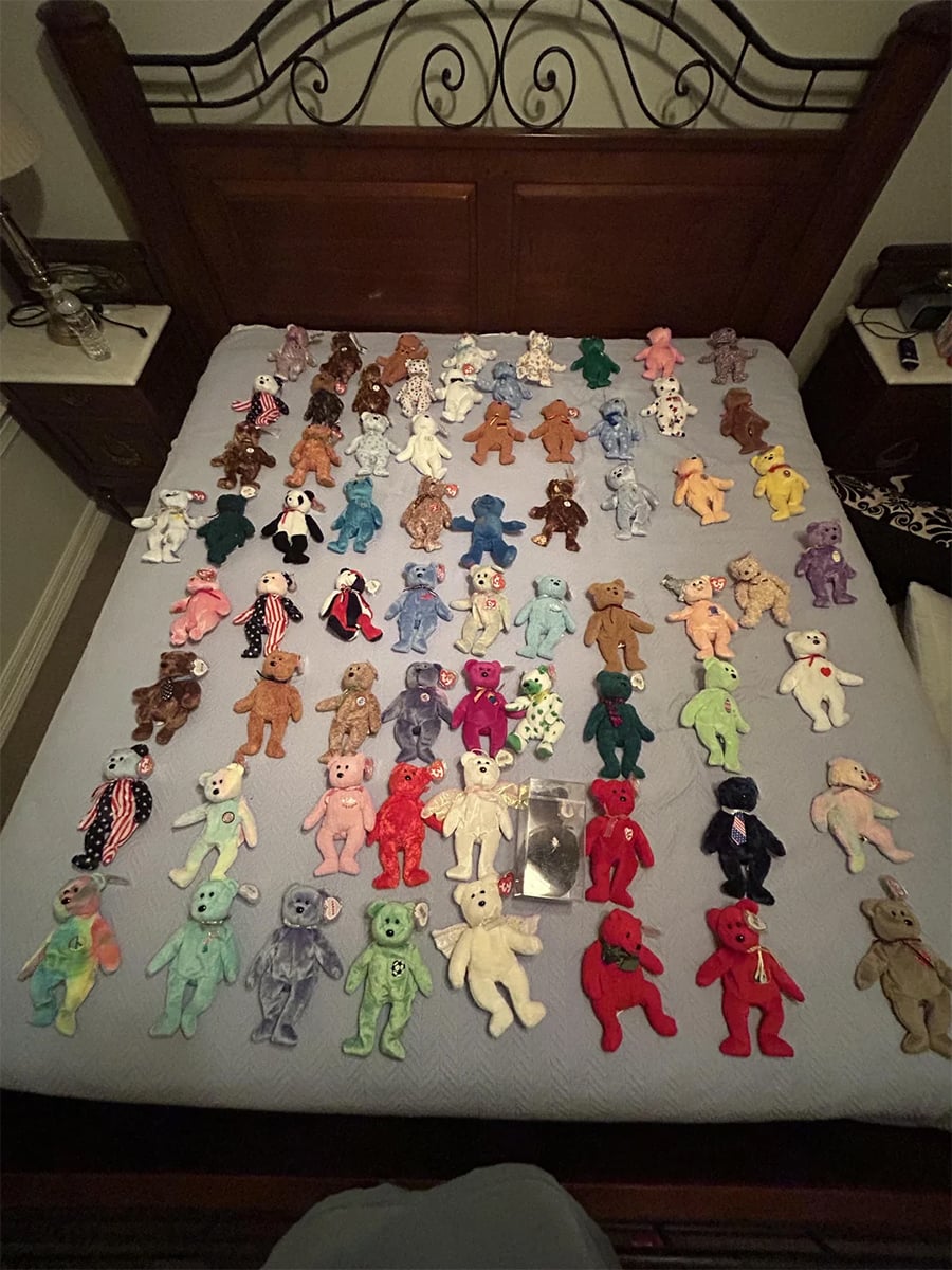 A collection of colorful Beanie Babies teddy bears is neatly arranged in rows on a bed with a wooden headboard. Some bears have unique patterns and accessories.