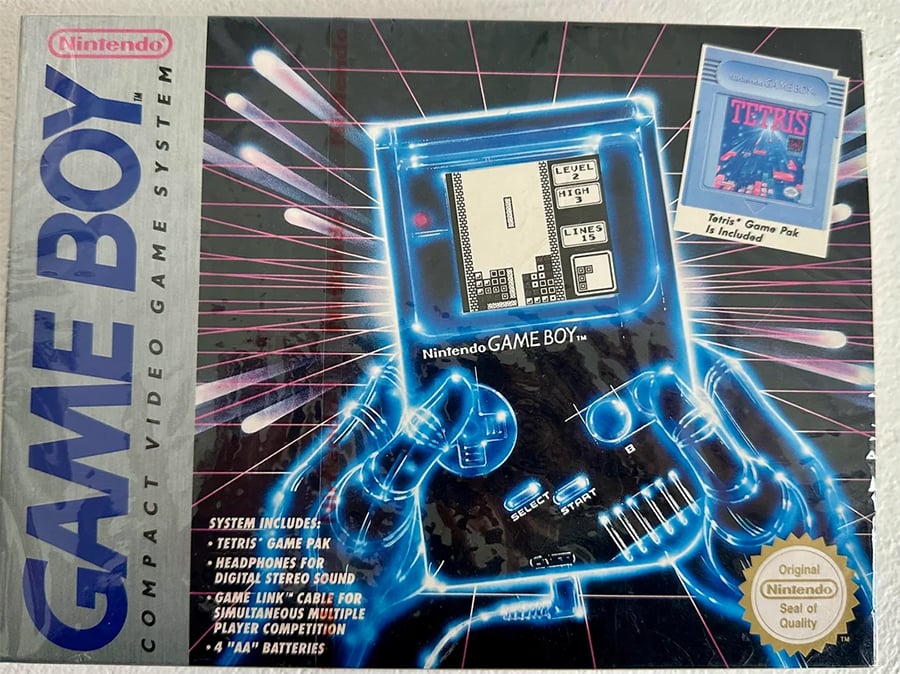 Nintendo Game Boy box showing a glowing illustration of hands holding a Game Boy, with “Tetris” displayed on its screen. The box lists included items and features the “Nintendo Seal of Quality” and Tetris Game Pak.