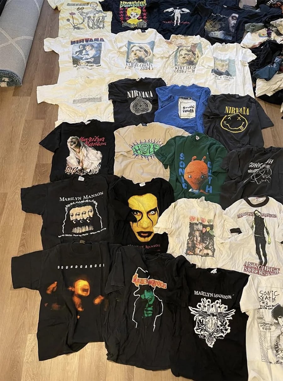 A collection of vintage band T-shirts, including Nirvana, Marilyn Manson, Soundgarden, Sonic Youth, and others, arranged neatly on a wooden floor.