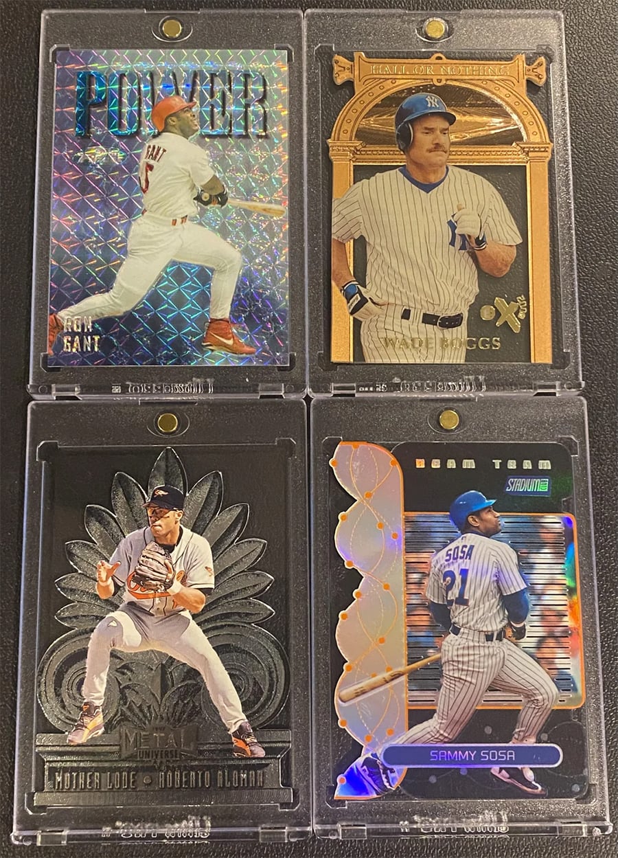 Four baseball trading cards in plastic sleeves featuring players in various action poses, each card with unique designs and holographic or metallic backgrounds.