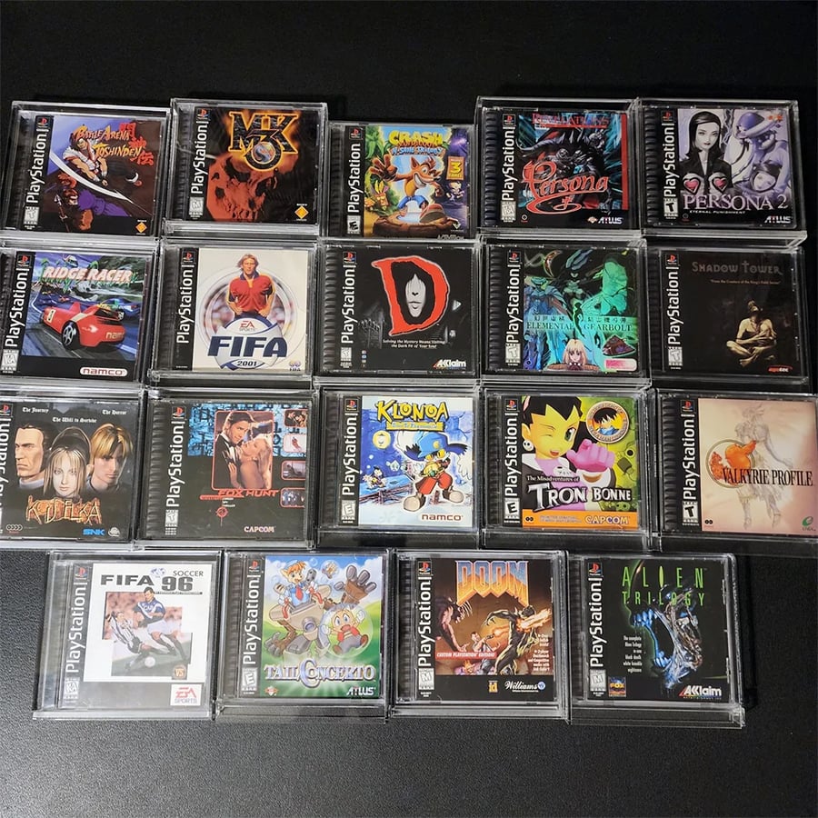 Twenty PlayStation 1 game cases arranged in a grid on a black surface, featuring titles like Crash Bandicoot, Persona 2, Ridge Racer, FIFA, Klonoa, Tron Bonne, and Doom.