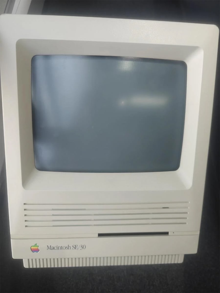 A vintage Macintosh SE/30 computer with a small, square CRT screen and beige casing, sitting on a dark surface.