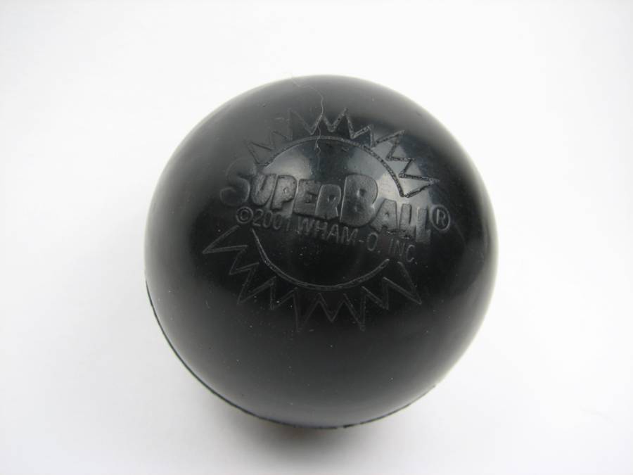 A black SuperBall with “SuperBall” and “©2001 WHAM-O, INC.” embossed on its surface, photographed on a white background.