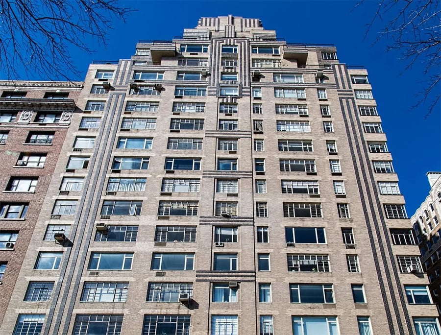 Tall Art Deco-style apartment building with symmetrical geometric patterns, numerous windows, and beige brick facade, set against a clear blue sky.