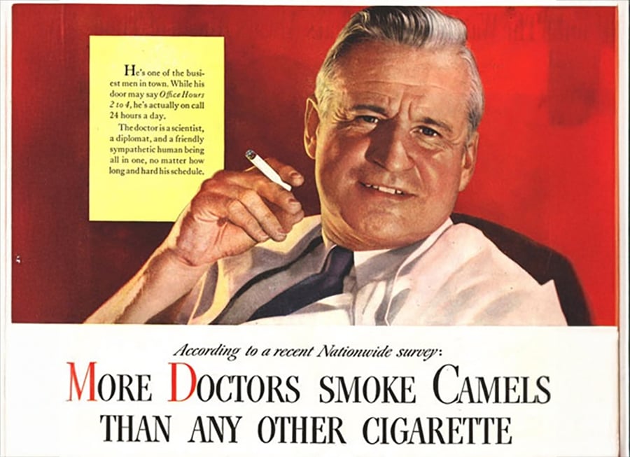 A smiling man in a white coat holds a cigarette. Text says, “More Doctors smoke Camels than any other cigarette,” suggesting doctors prefer Camel cigarettes. Additional text praises the man’s busy schedule.