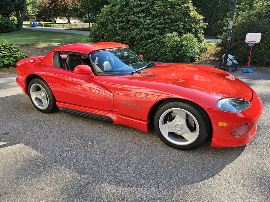 A bright red sports car, likely a Dodge Viper, parked on a driveway with green bushes and a basketball hoop visible in the background.