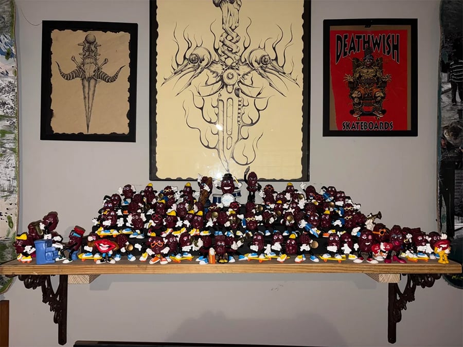 A shelf displays many collectible Mr. Potato Head toys in various poses. Above, framed art includes a large sword drawing and a Deathwish Skateboards poster. The wall is decorated with multiple pieces of art.