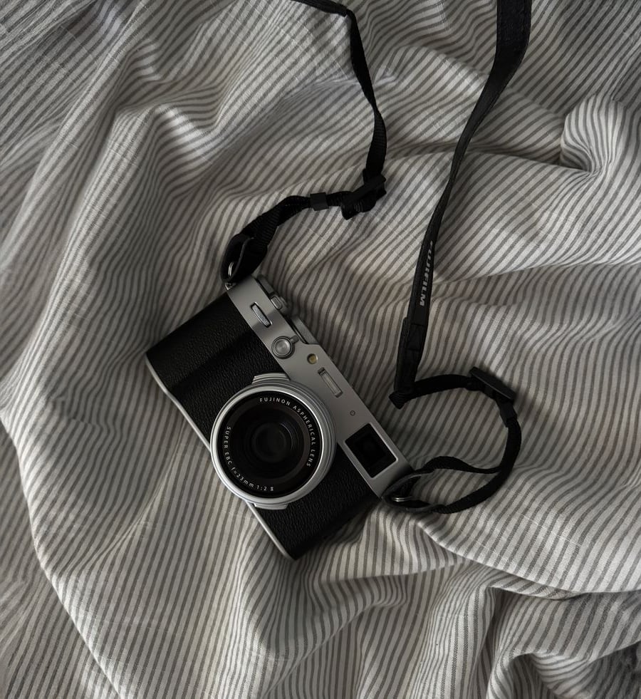 A vintage-style black and silver camera with a neck strap rests on a wrinkled, light gray and white striped fabric background.
