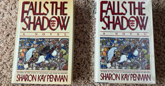 Two copies of the book “Falls the Shadow: A Novel” by Sharon Kay Penman are side by side on a tan carpet. Both covers feature medieval-style art with knights and horses.