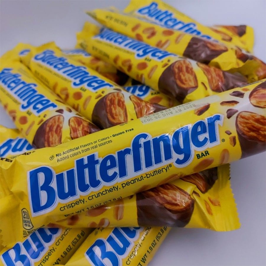 Several Butterfinger candy bars in yellow wrappers are stacked on top of each other. The text on the wrappers highlights that they are “crispy, crunchy, peanut-buttery.”