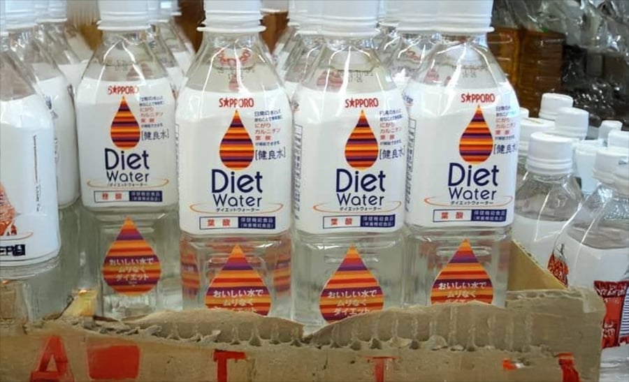 Plastic bottles labeled “Diet Water” with colorful designs are displayed in a cardboard box. Other bottled drinks are visible in the background on the store shelf.