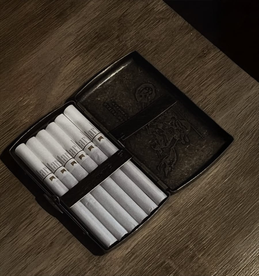 An open black cigarette case containing eight cigarettes sits on a wooden surface, with the lid showing an embossed design.