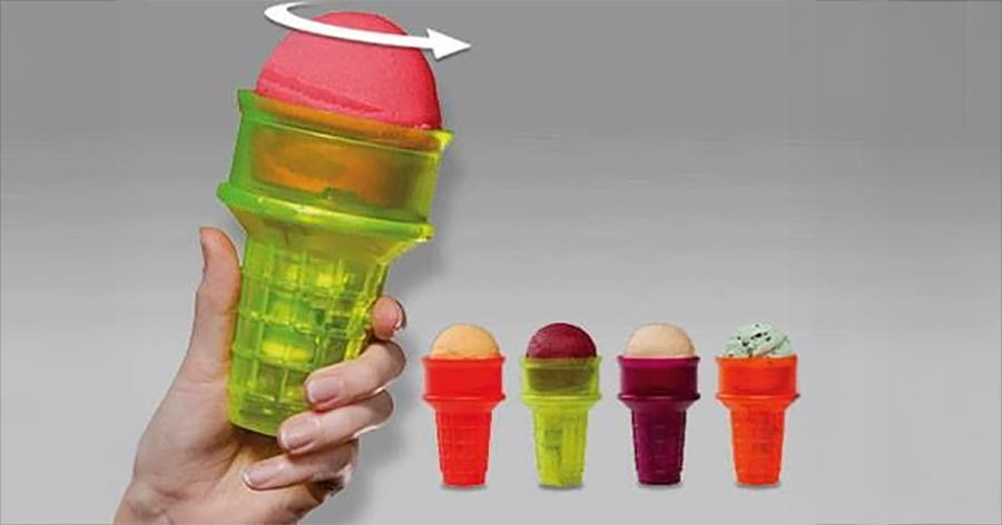A hand holds a green plastic ice cream holder with a red scoop on top, showing a rotating arrow. Three more colorful holders with ice cream scoops are lined up in the background.