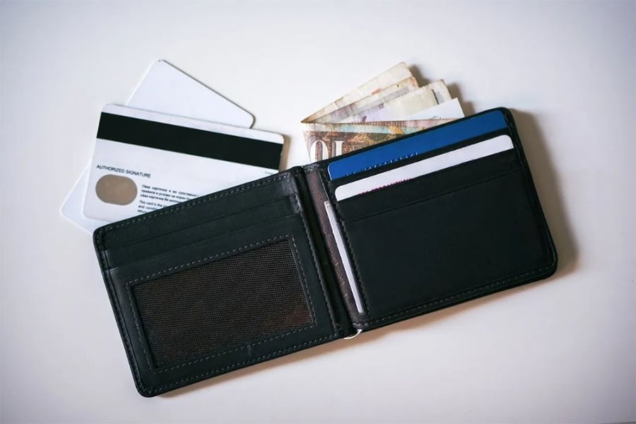 A black wallet with cards, cash, and banknotes partly visible, lying open on a white surface. Two cards are placed outside the wallet.
