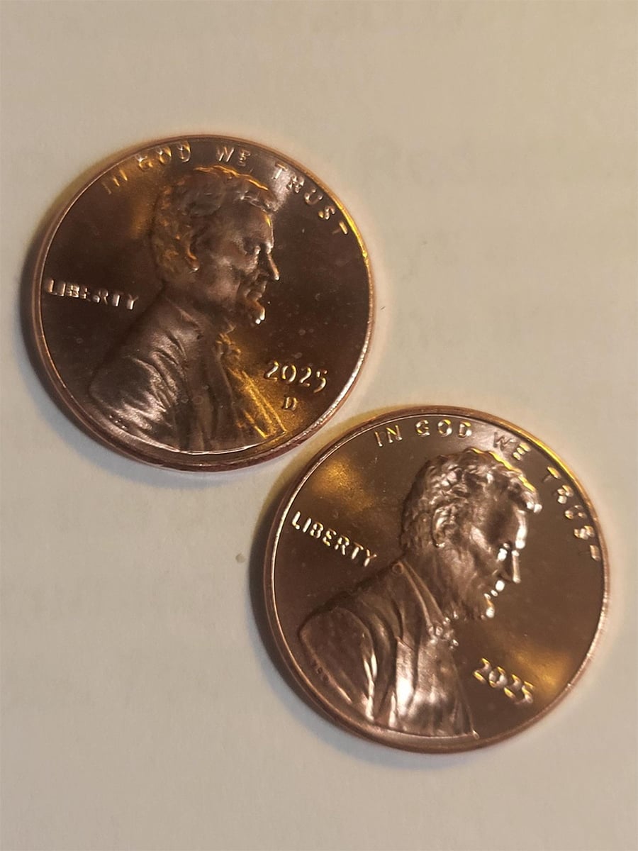 Two shiny 2023 US pennies featuring Abraham Lincoln, placed on a light surface. Both show the obverse side with “IN GOD WE TRUST,” “LIBERTY,” and the year “2023.”