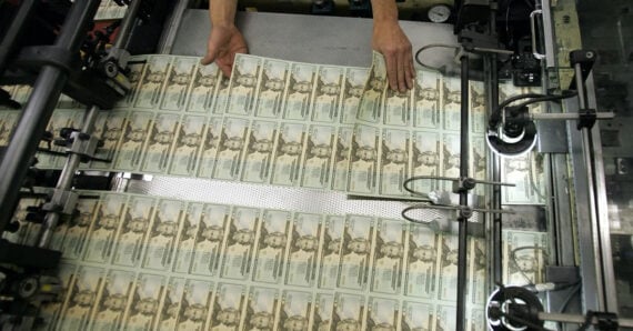 Sheets of U.S. Treasury checks being printed, with a person’s hands guiding the paper through a large industrial printing machine.