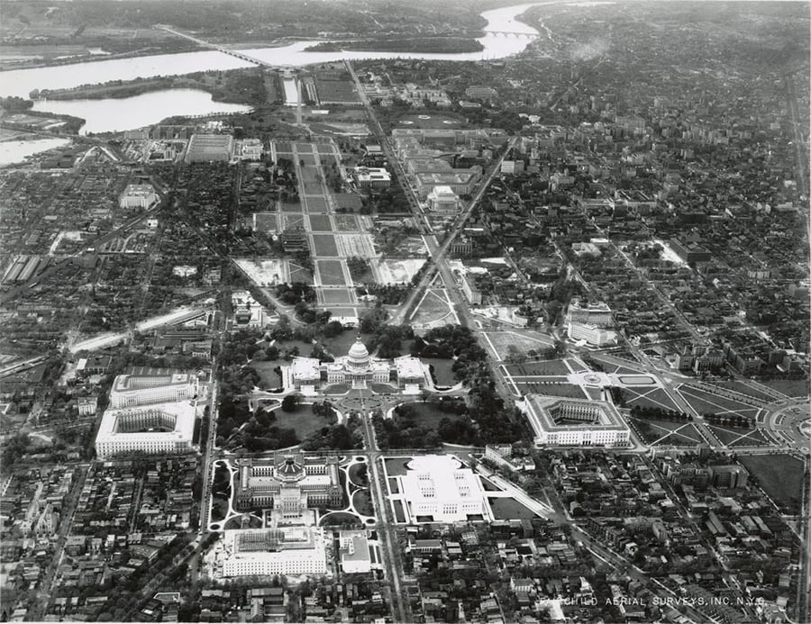 Aerial black and white view of Washington, D.C., showing the Capitol building, surrounding government buildings, and the National Mall extending toward the Potomac River.
