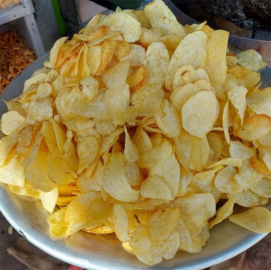 A large metal bowl filled with crispy, golden-yellow potato chips.