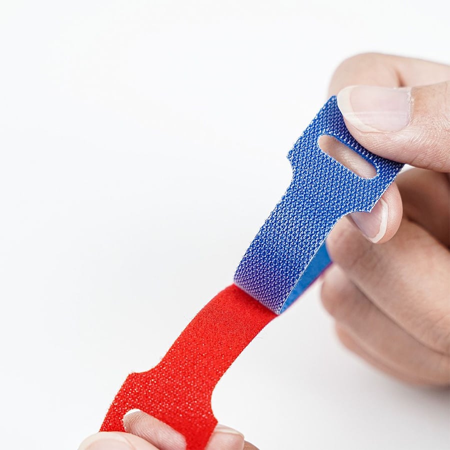 Two hands connect a blue and red fabric strap with hook-and-loop fasteners against a white background.