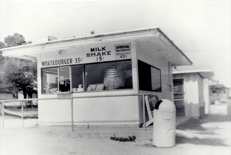 Black and white image of a small Whataburger stand with signs advertising burgers for 35 cents, milkshakes for 15 cents, and a special for 45 cents. A trash can is visible in the foreground.