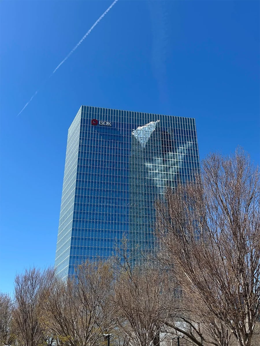 A tall glass office building with bare trees in front. The building reflects a white cloud and contrail in the blue sky. The “BB&T” logo is visible near the top corner of the building.