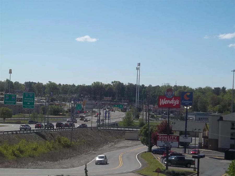 A busy intersection with cars, highway signs, a Wendy’s restaurant, a Comfort Inn hotel, and other businesses under a clear blue sky with some trees in the background.