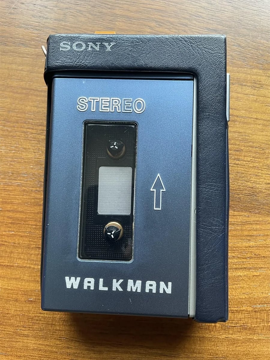 A vintage Sony Walkman cassette player with a blue and black exterior sits on a wooden surface. The words “SONY,” “STEREO,” and “WALKMAN” are visible on the device.