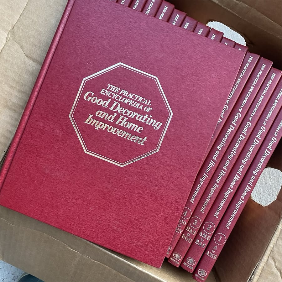 A set of red hardcover books titled “The Practical Encyclopedia of Good Decorating and Home Improvement” arranged in a cardboard box.