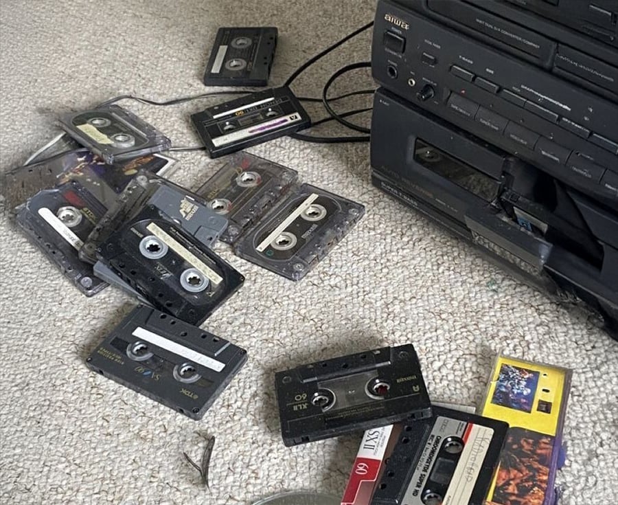 Several cassette tapes are scattered on a light-colored carpet next to a black stereo system, some tapes are open or partially unspooled.