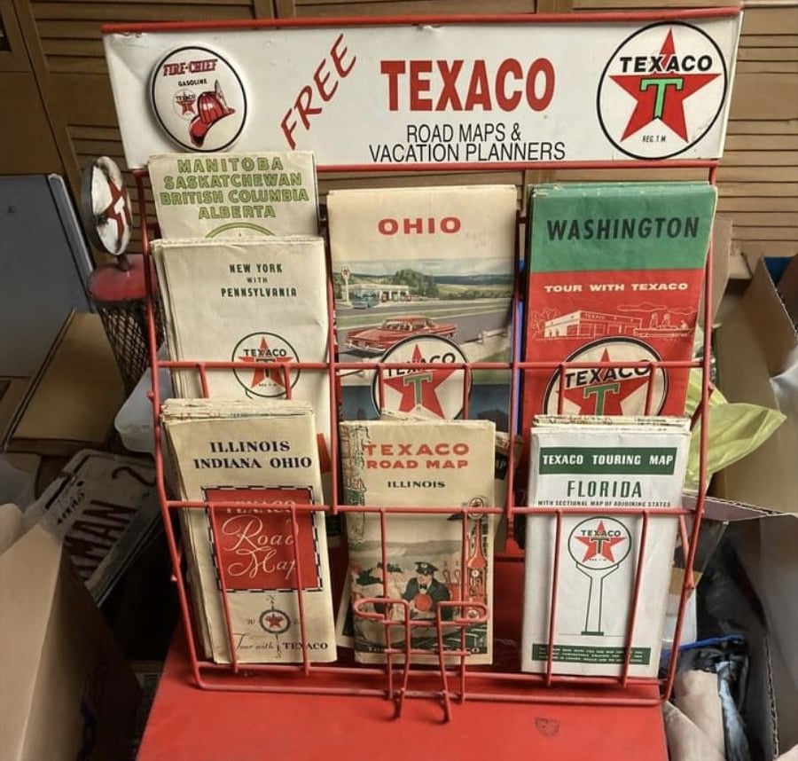 A metal rack displays vintage Texaco road maps for various U.S. states and Canadian provinces, with a sign reading “FREE TEXACO ROAD MAPS & VACATION PLANNERS” and prominent Texaco branding.