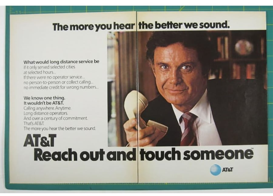 A man in a suit holds a white telephone receiver, smiling, beside AT&T text: “Reach out and touch someone.” The ad promotes AT&T long-distance service with a message about better communication.