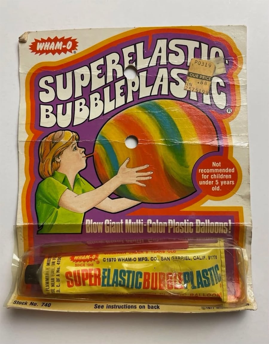Vintage Wham-O Super Elastic Bubble Plastic toy package with a colorful balloon illustration, a tube of plastic, and warnings. Child blowing up a multi-color bubble. Text notes not for children under 5 years old.