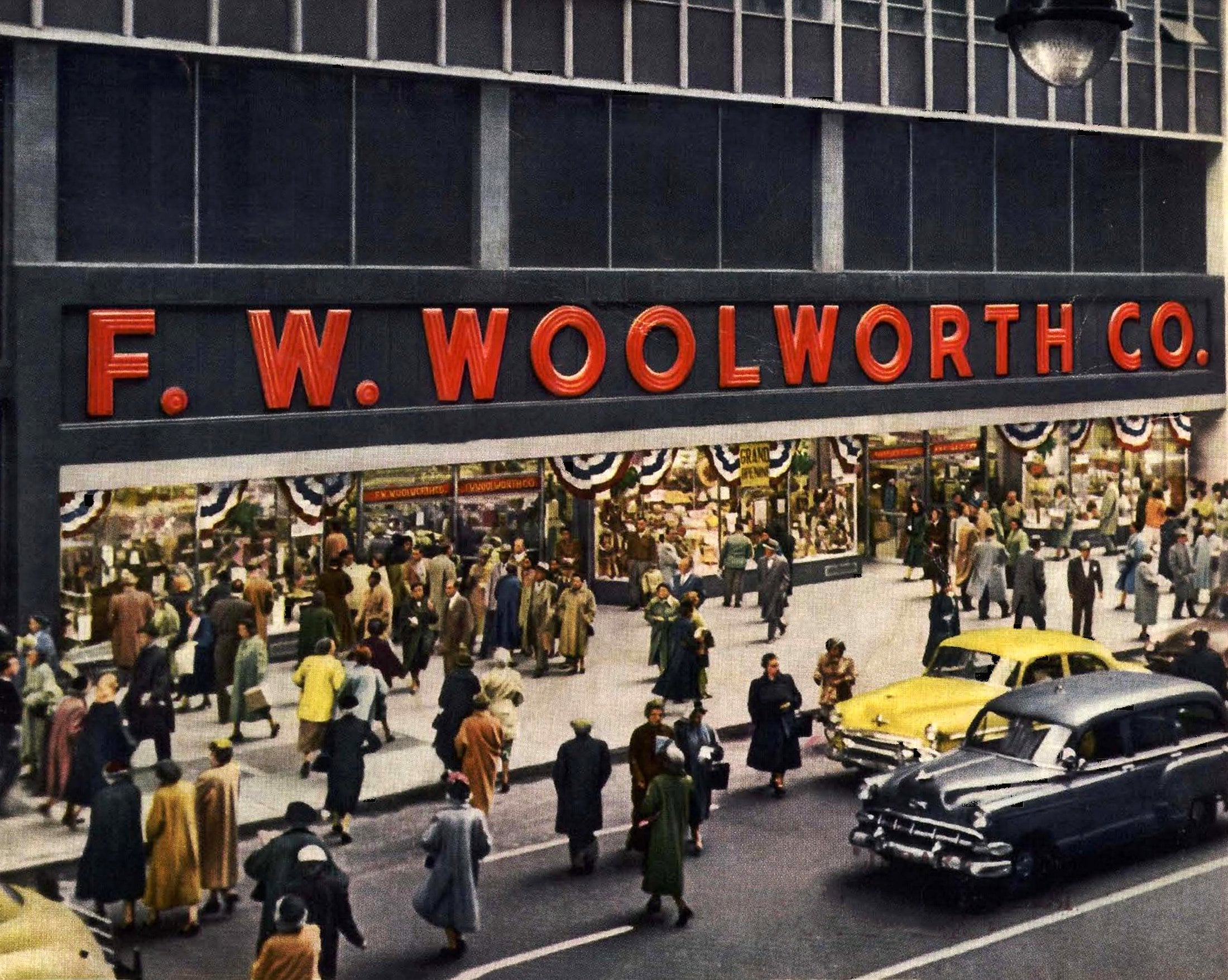 Crowds of people walk past the F. W. Woolworth Co. store, with large red signage, decorated windows, and classic cars parked along the busy street in front.