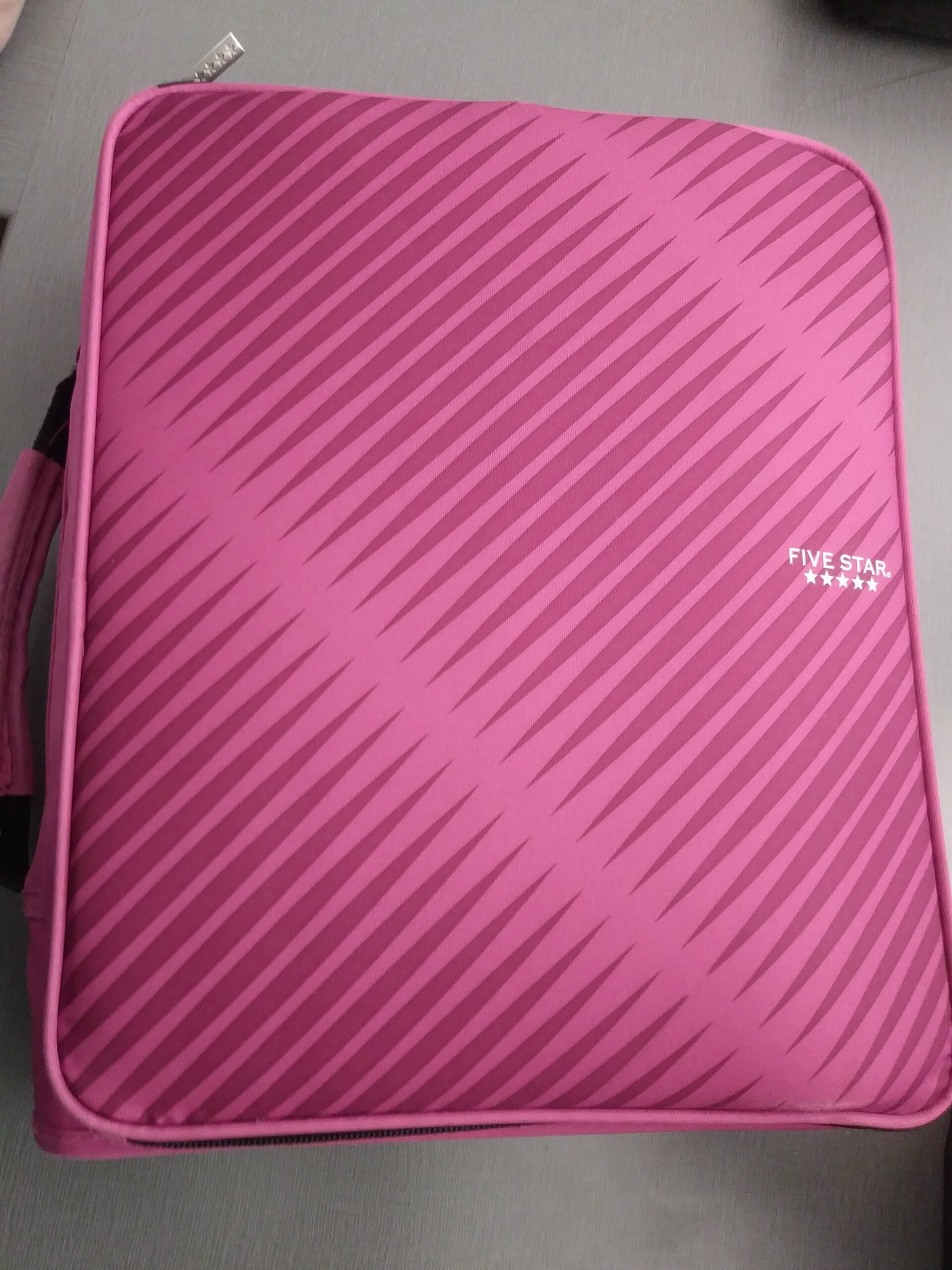 A pink Five Star binder with diagonal stripes, a zipper, and a handle, placed on a gray surface. The Five Star logo with three stars is visible in the upper right corner.