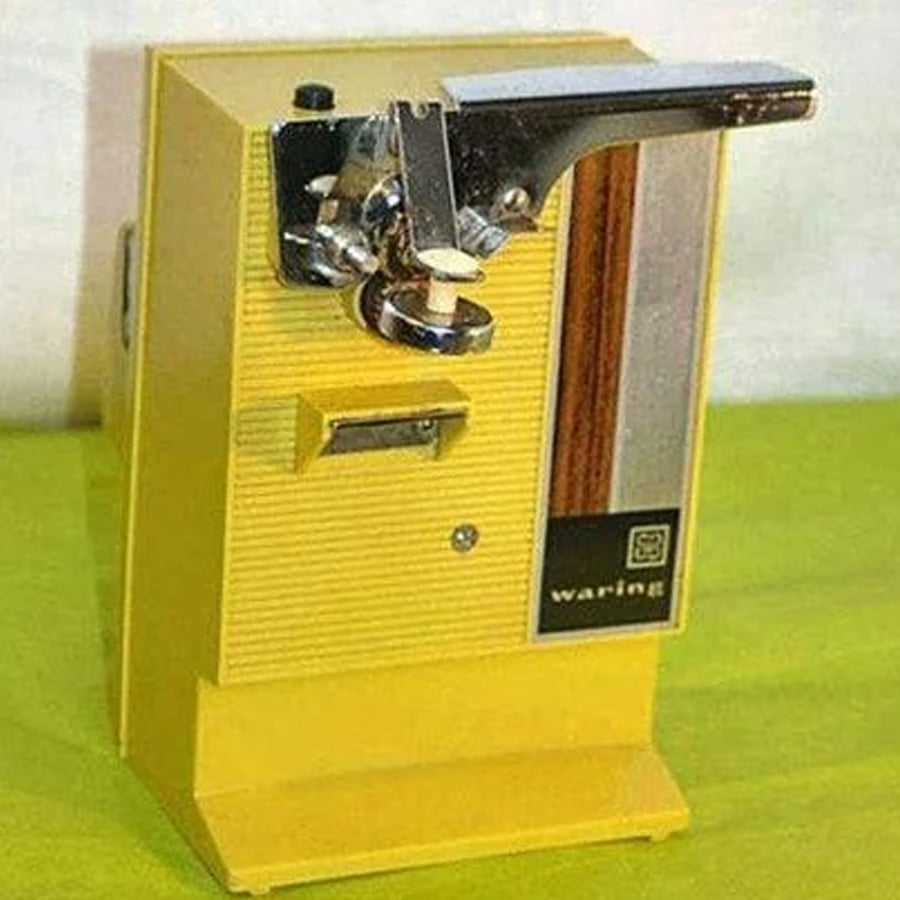 A vintage yellow electric can opener with a metal handle and “waring” label on the front, placed on a light green surface with a light background.
