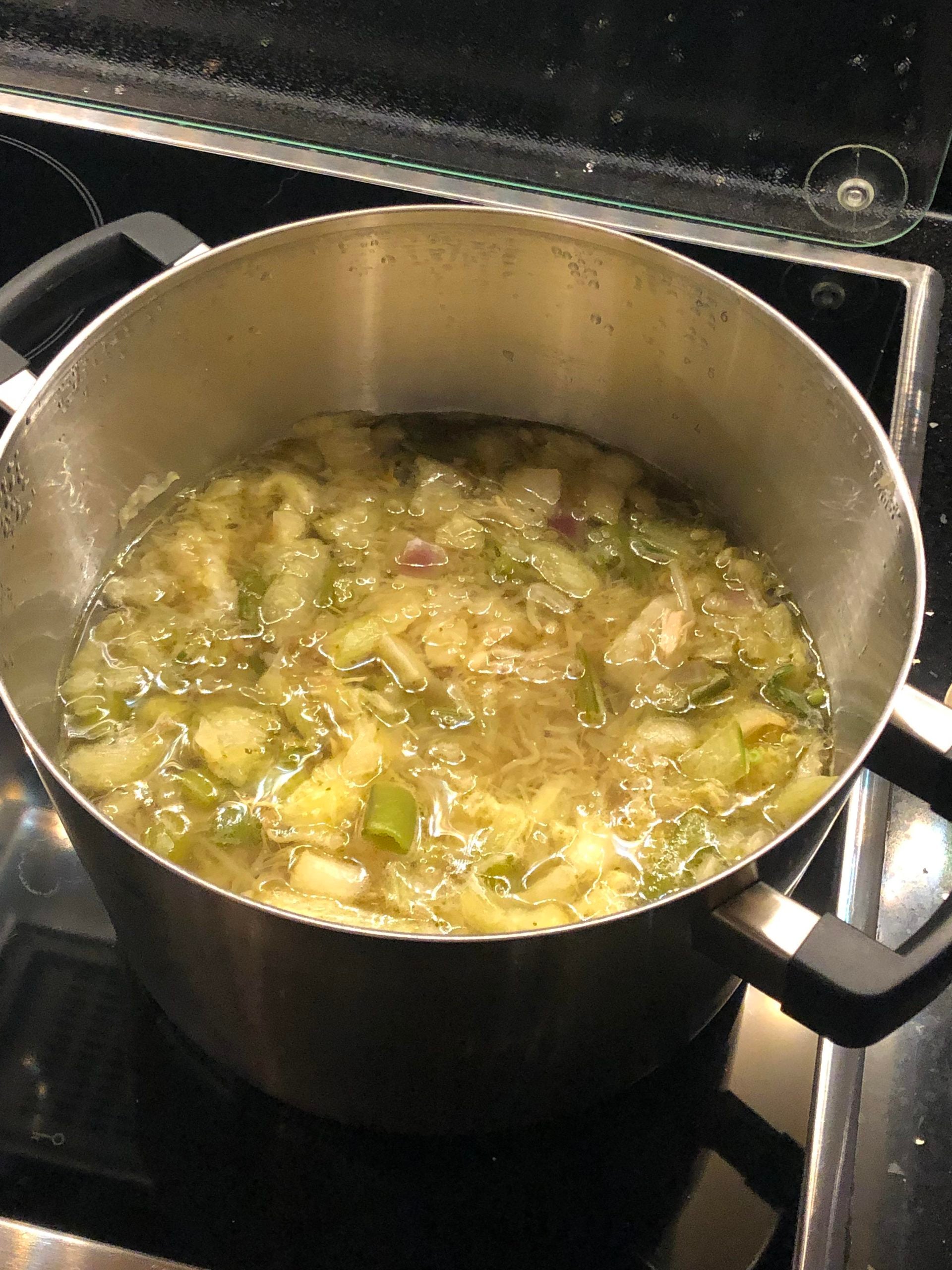 A large pot of homemade soup with visible vegetables and noodles simmers on a stovetop.