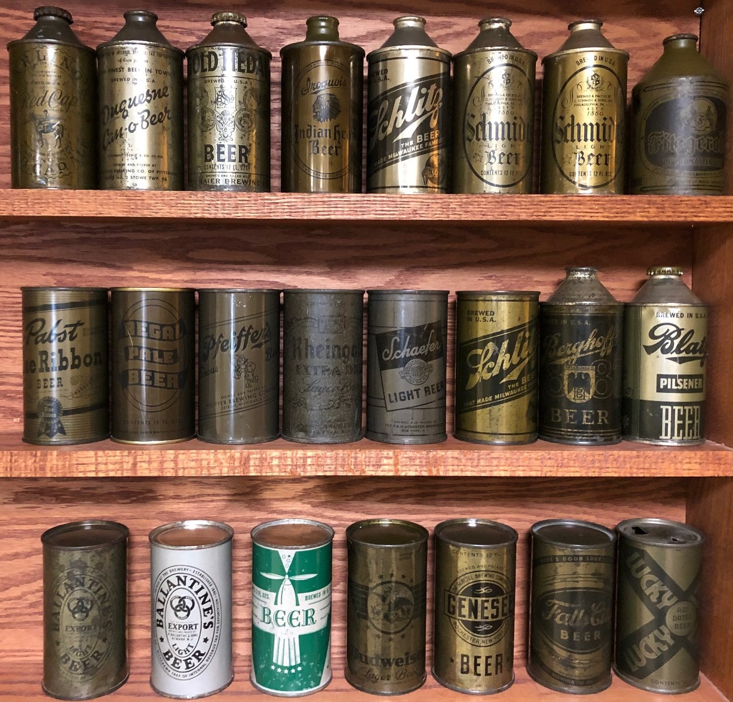 Rows of vintage beer cans with various labels and designs are displayed on wooden shelves. The cans are metallic with aging and retro branding, showing different beer names and logos.