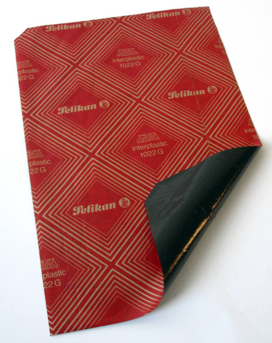 A sheet of red Pelikan interplastic 1022 G carbon paper, partially folded at the corner to reveal the black carbon side underneath.