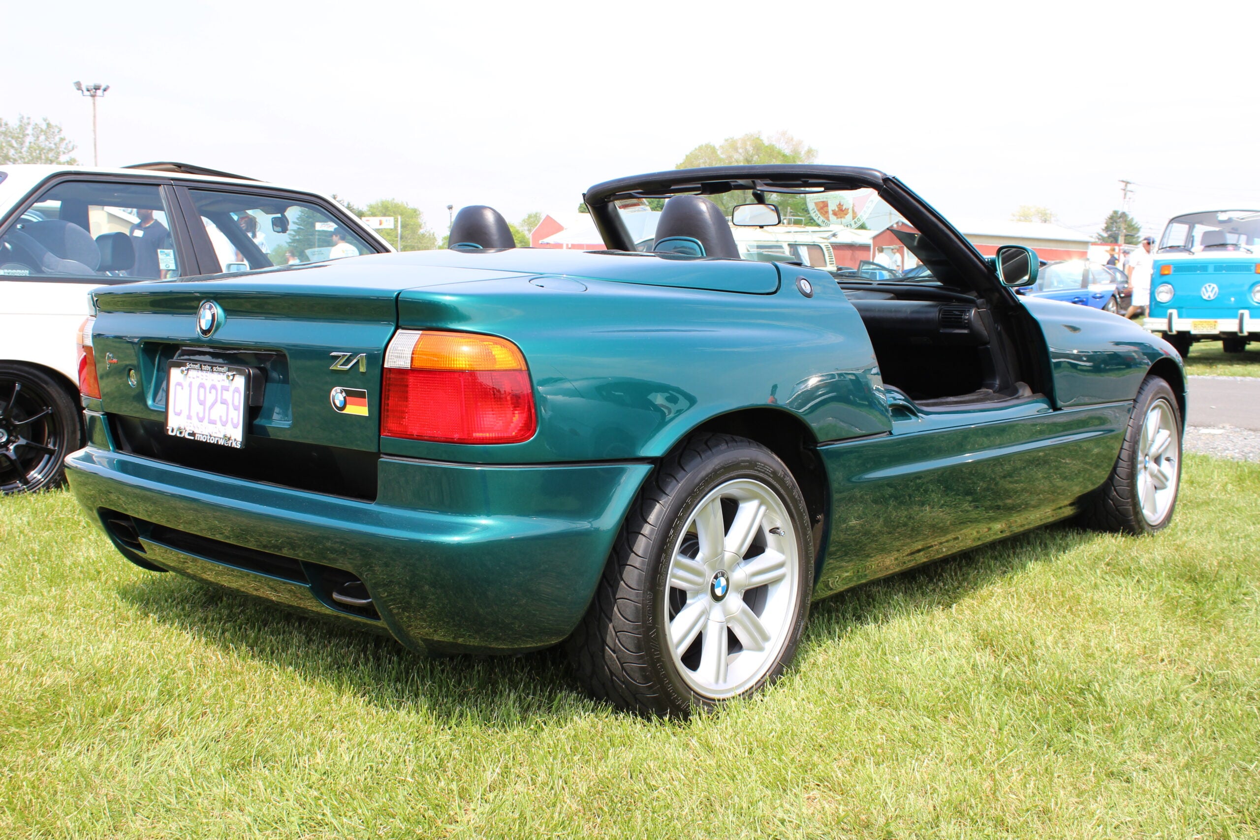 A green BMW Z1 convertible with its top down is parked on grass at a car show, showcasing its distinctive drop-down doors and sporty design.