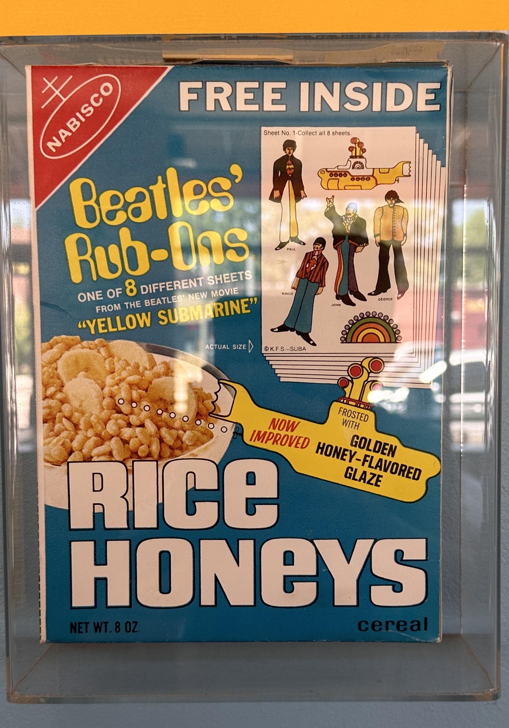 A vintage Rice Honeys cereal box advertises Beatles “Yellow Submarine” rub-on transfers and features an image of the Beatles as cartoon characters, with a bowl of cereal shown at the bottom.