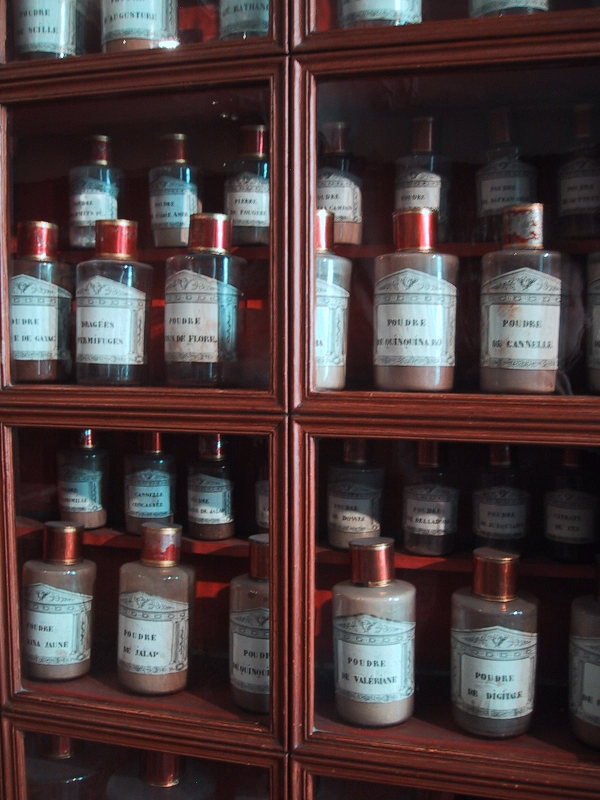 Glass cabinets filled with vintage apothecary jars and bottles with old-fashioned labels, organized neatly in rows and columns.